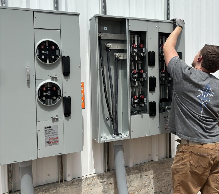 Professional electrician mounting a modern 200-amp electrical service panel with circuit breakers on a home's exterior wall